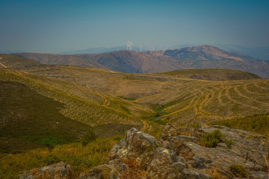 Turismo Sustentável — Panoramic view of rolling hills with wind turbines on the distant mountains under a bright sky.