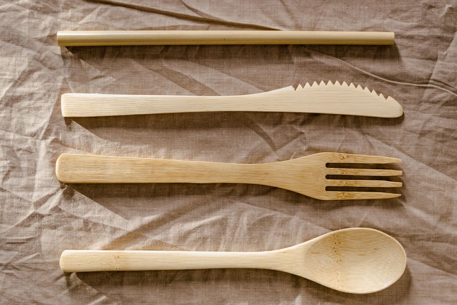 Turismo Sustentável — Close-up of reusable wooden utensils including spoon, fork, knife, and straw on linen fabric.