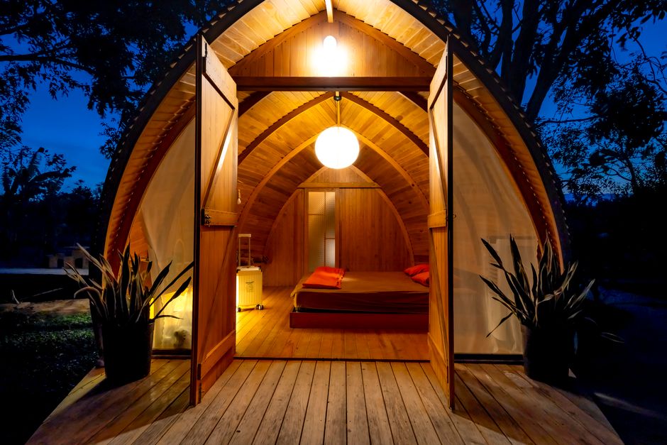 Turismo Sustentável — Warmly lit wooden cabin with open doors at night, showcasing cozy interior and unique architecture.
